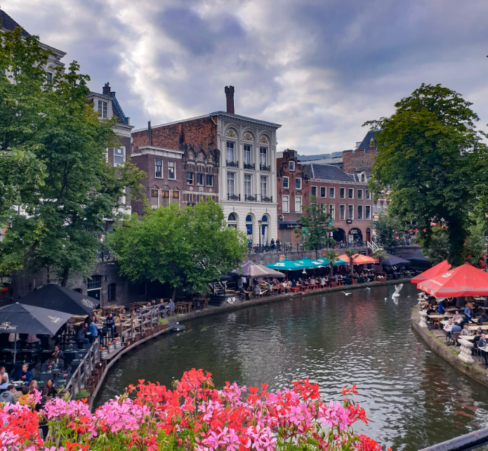 Een gracht midden in een stad met veel mensen en bloemen.